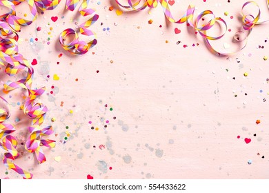 Delicate pink party background with colorful streamers for celebrating a carnival forming a border around copy space with scattered confetti
