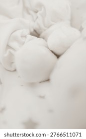 A delicate top view of a newborn's tiny feet wrapped in soft white cotton. The feet rest on a clean white blanket subtly patterned with light grey stars. Focus is on the toes and the softness of the textile. Evokes a sense of peace, warmth, and sleeping serenity. Natural, bright light.