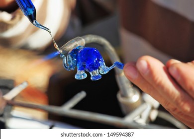 Delicate work of the glass blower. The Artist-glass blower produces a graceful tiny figure of an elephant from color glass