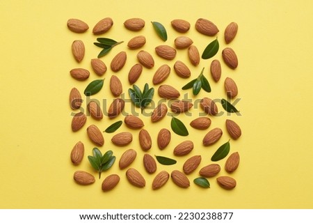 Delicious almonds and fresh leaves on yellow background, flat lay