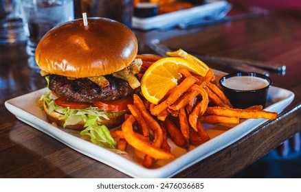 A delicious Angus beef cheeseburger with a side of crispy sweet potato fries with dipping sauce and on orange slice on a table. - Powered by Shutterstock