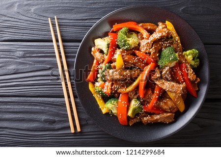 delicious Asian teriyaki beef with red and yellow bell peppers, broccoli and sesame seeds close-up on a plate on the table. Horizontal top view from above

