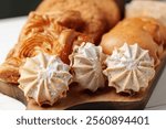 Delicious assortment of baked goods displayed on a wooden board, featuring meringue cookies and pastries in a cozy bakery setting