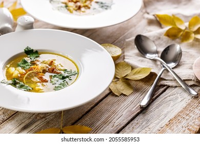 Delicious Autumn Soup With Chanterelles And Fresh Herbs. Seasonal Dish With Edible Mushrooms. White Plate And Cutlery On A Rustic Background. Food Still Life. Organic Wild Foods.