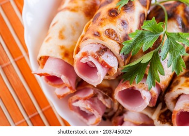 Der köstliche Speck ist in Pfannkuchen mit einer Tube eingewickelt, neben einer grünen Petersilie. Essen in einem weißen Teller auf einer orangefarbenen Bambusmatte.