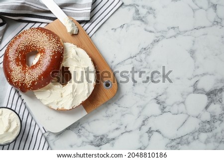 Delicious bagel with cream cheese on white marble table, flat lay. Space for text
