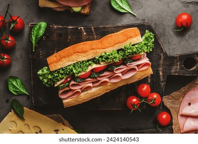 Delicious baguette sandwich with ham, bacon, cheese, lettuce, tomatoes, sausage, gammon on cutting board with herb and spices over on dark background. Meat food, top view, flat lay, toning - Powered by Shutterstock