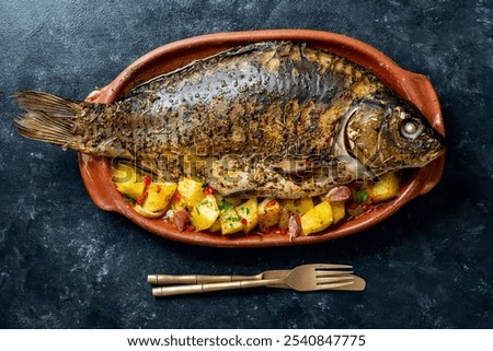 Delicious baked carp fish with spices in a clay plate and fried vegetables, close up, top view