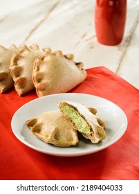 Delicious Baked Empanada Cut In Half On A Plate, On Top Of A Red Fabric Placemat, With Other Pasteis On Background