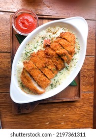 A Delicious Baked Rice Topped With Mozarella Cheese And Chicken Katsu Served With Tomato Sauce Isolated On Wooden Background