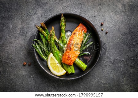 Delicious baked salmon with asparagus, lemon slices and spices on black background. Top view.