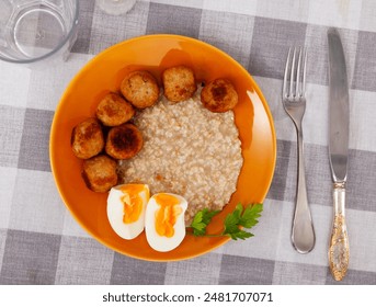 Delicious balanced meal of boiled eggs with creamy yolks, savory meatballs, and hearty oatmeal, served on vibrant orange plate over checkered tablecloth - Powered by Shutterstock