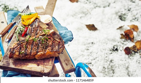 Delicious Barbecued Marinated T-bone Steak Seasoned With Herbs And Served With Grilled Vegetables On A Wooden Board On A Sled At A Winter Barbecue Outdoors In The Snow With Copy Space