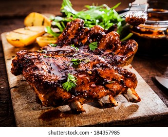 Delicious barbecued ribs seasoned with a spicy basting sauce and served with chopped fresh herbs on an old rustic wooden chopping board in a country kitchen