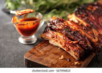 Delicious barbecued ribs seasoned with a spicy basting sauce and served with chopped fresh vegetables on an old rustic wooden chopping board in a country kitchen