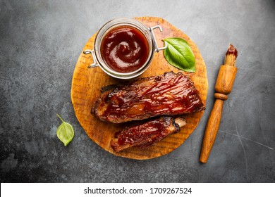 Delicious BBQ Baby-back Ribs With Tangy Sauce And A Basting Brush On Black Background, Top View