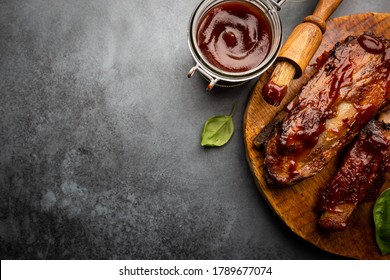 Delicious BBQ Baby-back Ribs With Tangy Sauce And A Basting Brush On Black Background, Top View