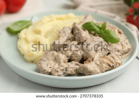 Delicious beef stroganoff with mashed potatoes and basil on white table, closeup