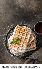 Delicious belgian waffles in stack with powdered sugar on a plate on dark background top view. Vertical