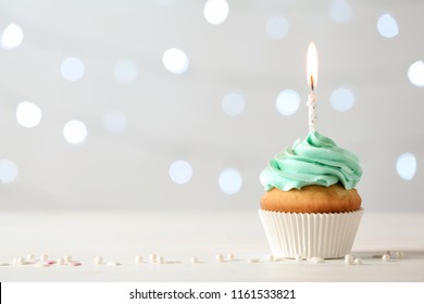 Delicious birthday cupcake with burning candle and space for text on blurred lights background