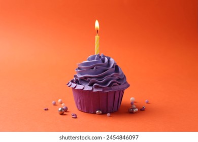 Delicious birthday cupcake with burning candle and sprinkles on coral background - Powered by Shutterstock