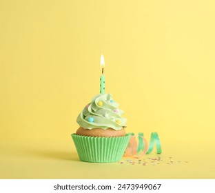 Delicious birthday cupcake with burning candle, sprinkles and streamers on yellow background - Powered by Shutterstock