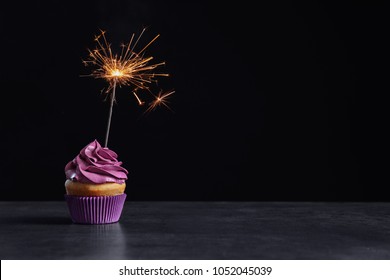 Delicious Birthday Cupcake With Sparkler On Table Against Black Background