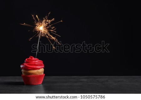 Delicious birthday cupcake with sparkler on table against black background