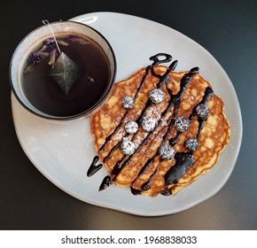 Delicious Blue Berry Pancakes With Fresh Blueberries On Top And Chocolate Sauce Serve With Hot Tea On The  Gray Plate On The Dark Table. Selective Focus