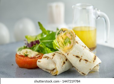 Delicious breakfast with eggs burrito with little salad and juice, toasted, crispy bacon, English muffins, ham, poached eggs, and delicious buttery hollandaise sauce.wooden background . Top view
