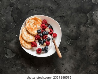 Delicious breakfast - Greek yogurt with berries and mini pancakes on a dark background, top view - Powered by Shutterstock