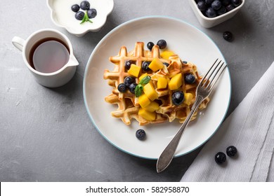 Delicious Breakfast With Homemade Waffles, Fresh Mango, Blueberries, Maple Syrup And Yogurt; Overhead Shot