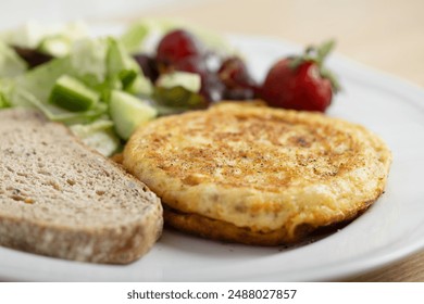 A delicious breakfast plate featuring a golden-brown omelette, two slices of whole grain bread, a fresh mixed green salad, red grapes, and a ripe strawberry. A nutritious and balanced meal ideal. - Powered by Shutterstock