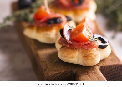 Delicious breakfast sandwiches with salami, tomato, olives and thyme on rustic wooden board