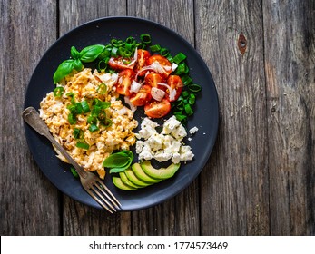 Delicious breakfast - scrambled eggs with fried sausages, cottage cheese, and avocado served on black plate on wooden table  - Powered by Shutterstock