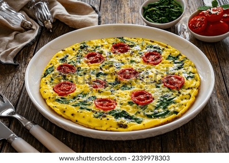 Delicious breakfast - scrambled eggs with spinach and cherry tomatoes on wooden table