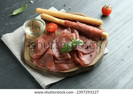 Delicious bresaola, tomato, grissini sticks and basil leaves on grey textured table