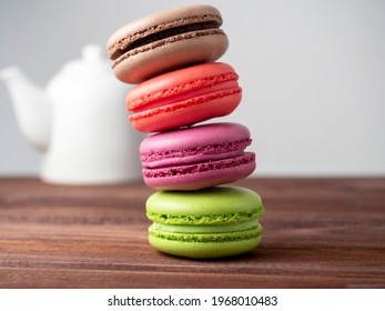 Delicious bright macaroons are stacked in a pyramid on a wooden background. In the background is a white teapot