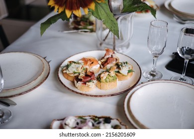 Delicious Bruschettas With Different Ingredients On A White Plate. Guacamole With Shrimp, Prosciutto, Salmon And Dorblu Cheese. Outdoor Feast On Holiday. Party