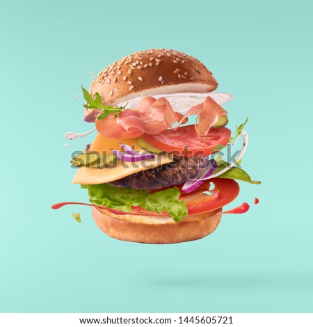 Delicious burger with flying ingredients isolated on turquoise background