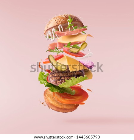 Delicious burger with flying ingredients isolated on pink background