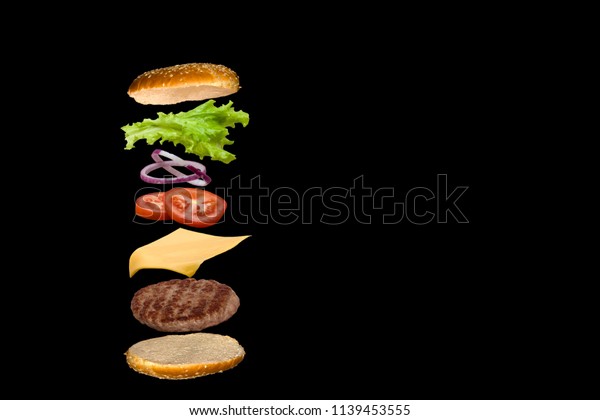 Delicious burger with flying ingredients\
isolated on black\
background.
