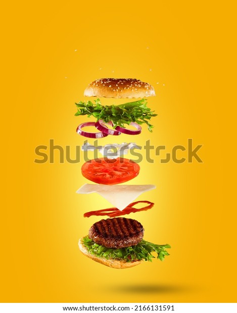 Delicious burger with\
flying ingredients  on a yellow background . Copy space for text,\
high resolution\
image.