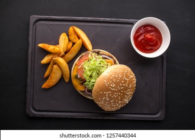 Delicious Burger With French Fries And Ketchup On Stone Plate On Black Background Top View