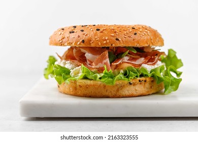 Delicious burger with prosciutto, cream cheese and lettuce for breakfast, sandwich, bagel with ham, close up - Powered by Shutterstock