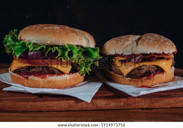 Delicious burgers with Bacon and cheddar\
cheese and with lettuce, tomato and red onion and bacon on homemade\
bread with seeds and ketchup on a wooden\
surface.
