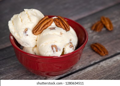 Delicious butter pecan ice cream served in a red bowl. Vintage wooden table background.