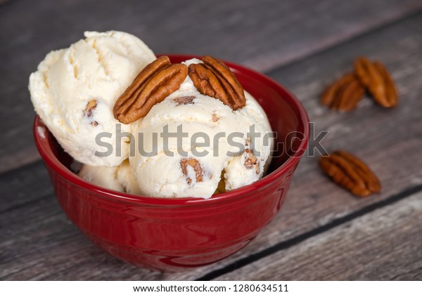 Delicious butter pecan ice cream served in a\
red bowl. Vintage wooden table\
background.