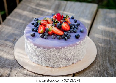 Delicious cake glazed with chocolate mirror lavender glaze, decorated with strawberries and blueberries on a wooden background