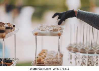 A lot of delicious cakes and desserts put up for guests. Delicious wedding reception candy bar dessert table. woman hands of a waiter prepare food for a buffet table in a restaurant - Powered by Shutterstock